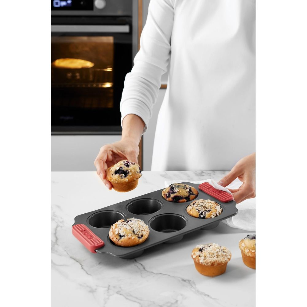 Eine Person nimmt einen Blaubeermuffin aus einer Muffinform. Ein Ofen ist im Hintergrund zu sehen.