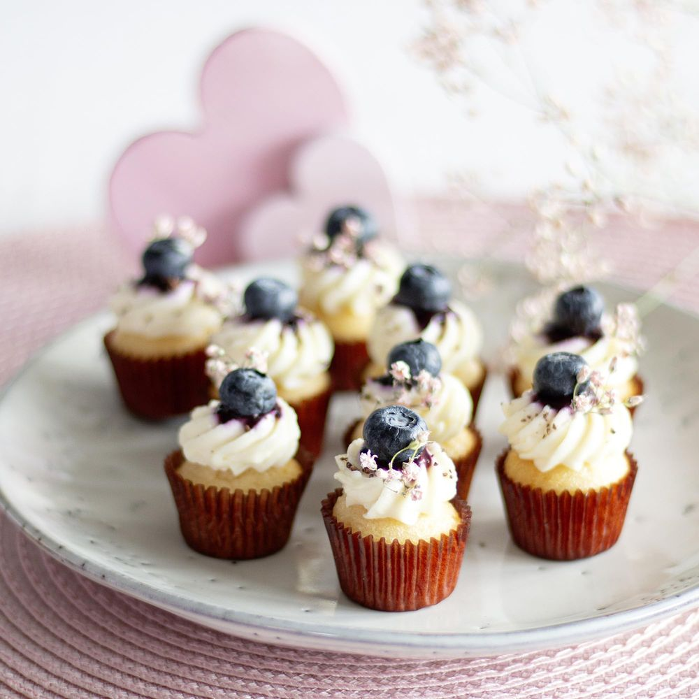 Mini cupcakes avec glaçage blanc, garnies de myrtilles et de fleurs roses.