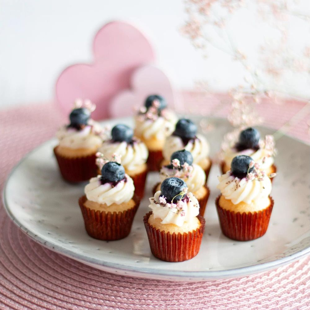Mini cupcakes avec glaçage blanc, myrtilles et fleurs roses sur une assiette.