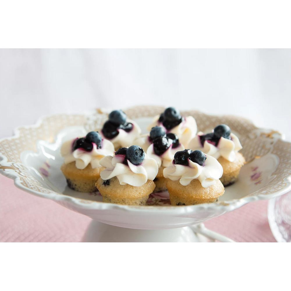 Mini cupcakes garnis de glaçage blanc et de myrtilles, sur une assiette décorative.