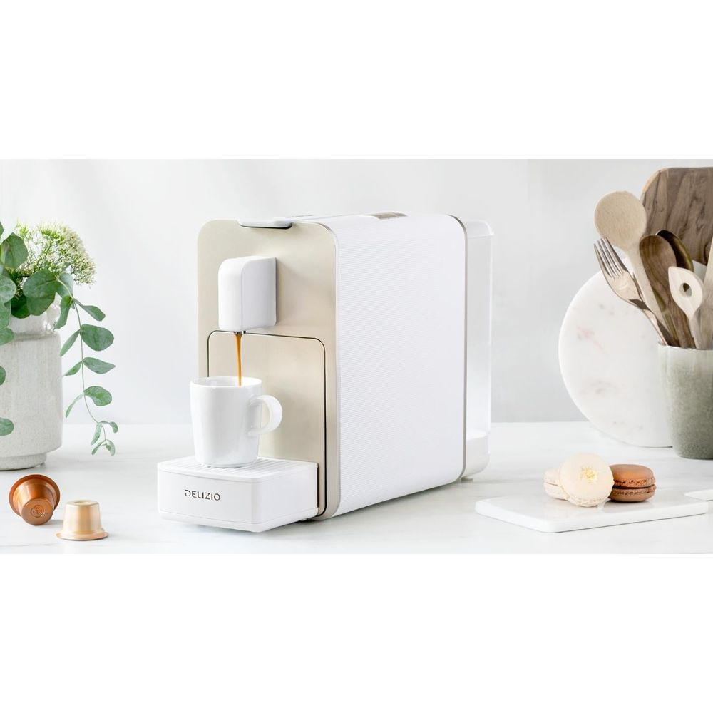 Une machine à café blanche prépare du café dans une tasse blanche. Des capsules de café sont à proximité.