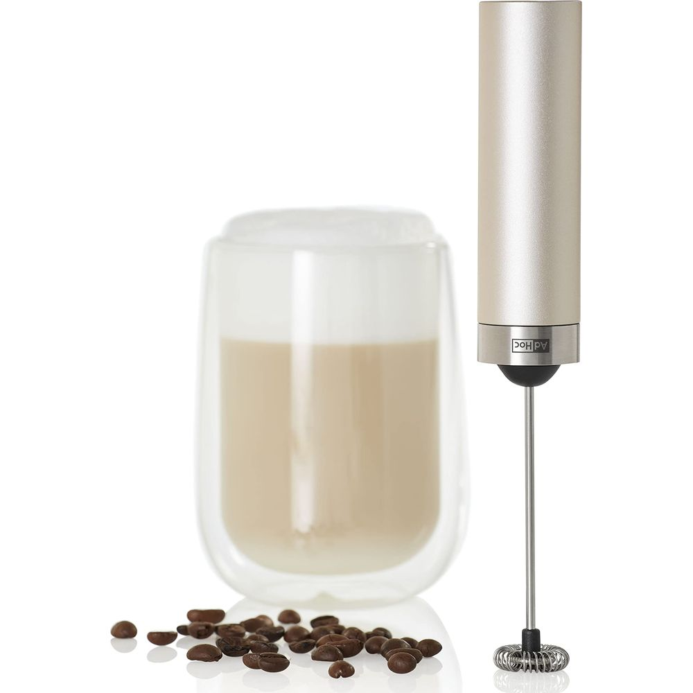Un mousseur à lait à côté d'un verre de latte macchiato avec des grains de café.
