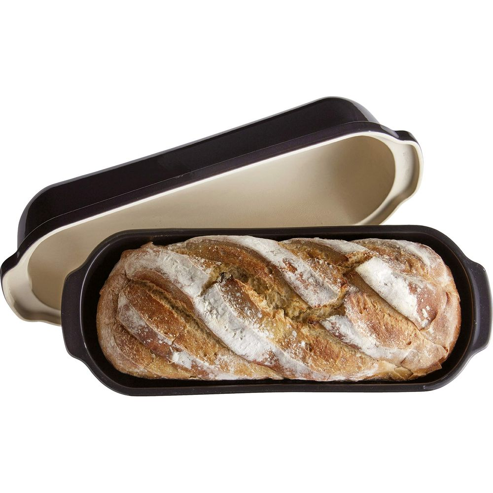 Un pain brun doré saupoudré de farine dans une cocotte à pain foncée avec couvercle.