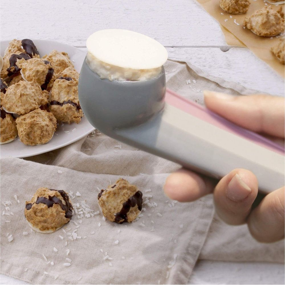 Une main utilise une cuillère à biscuits avec de la pâte pour former des macarons coco.