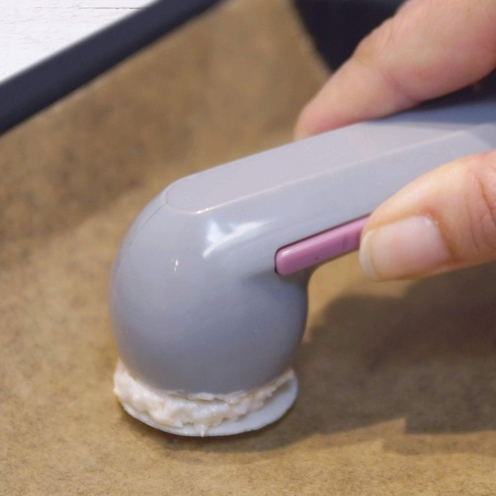 Une main presse un outil gris à bouton rose sur une garniture blanche sur papier sulfurisé.