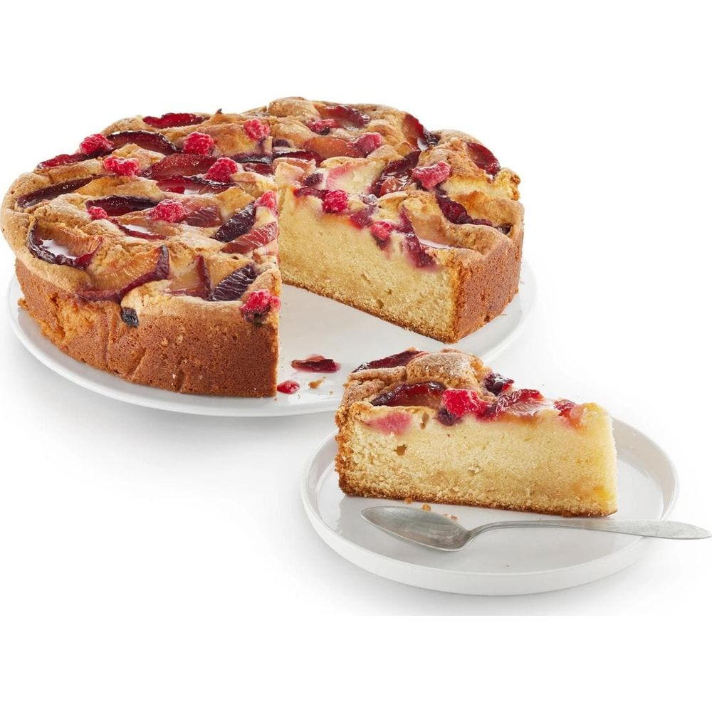 Gâteau aux prunes et framboises sur assiette blanche avec une part sur une petite assiette.