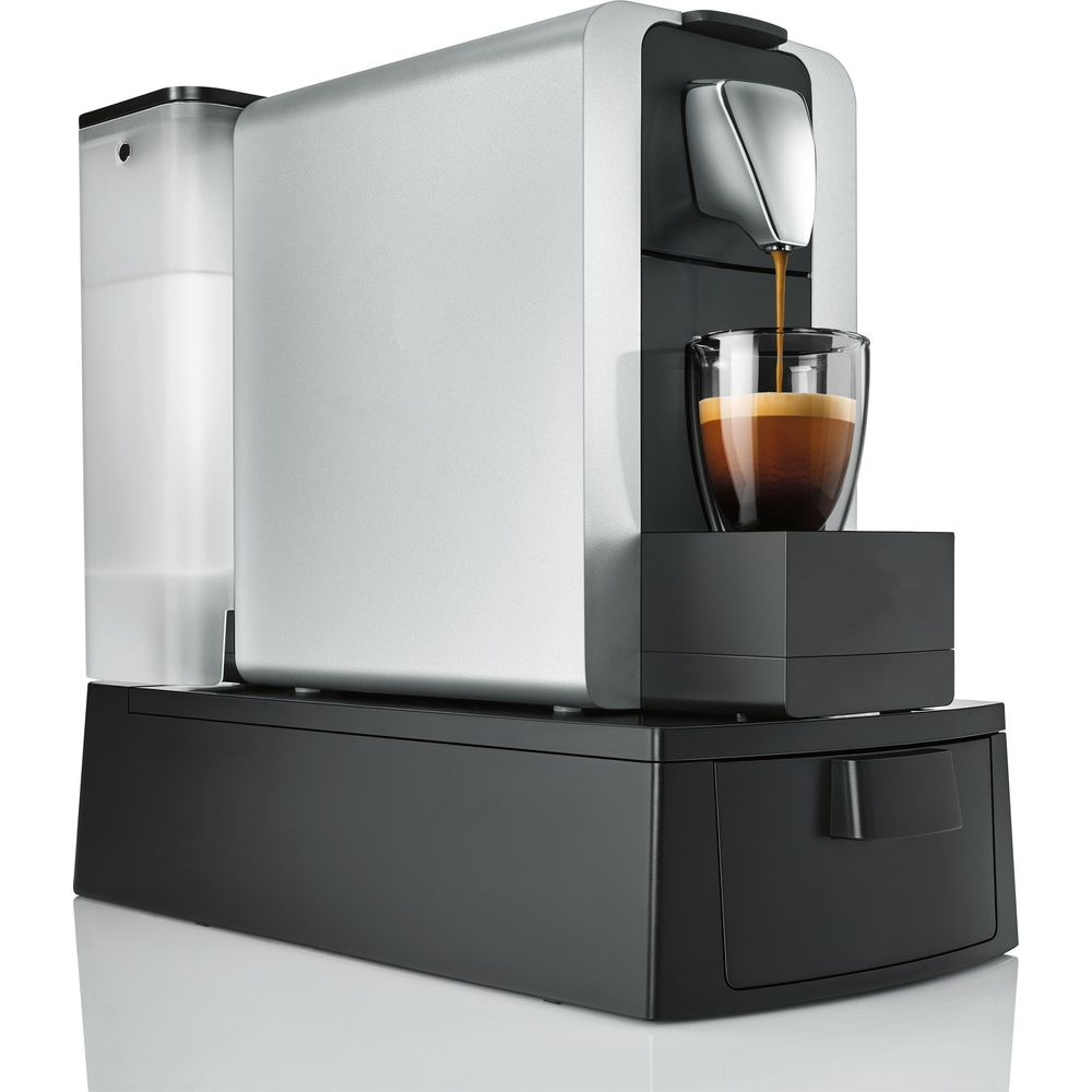 Eine silberne Kaffeemaschine brüht Espresso in eine klare Glastasse auf schwarzem Sockel.