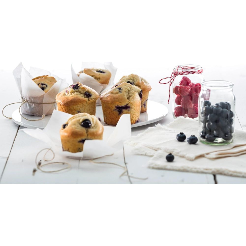 Mehrere Blaubeermuffins auf weißem Tisch mit zwei Gläsern Beeren.