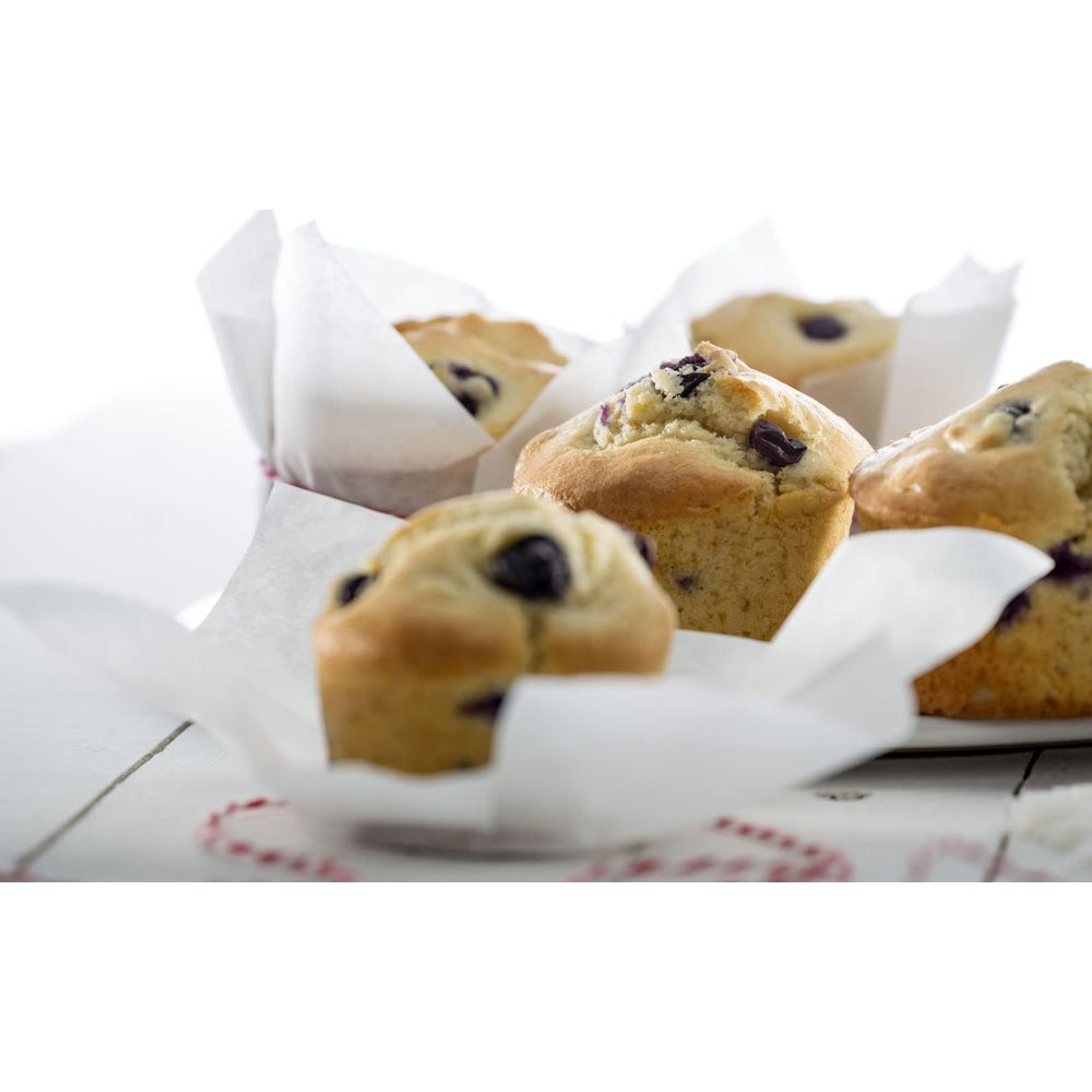 Fünf Blaubeermuffins in weißen Papierförmchen auf einem Holztisch.