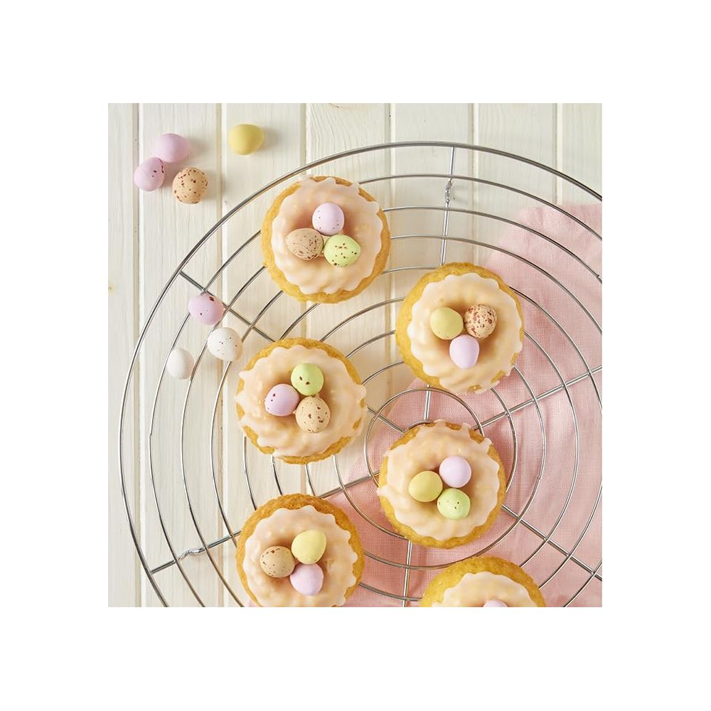 Sechs verzierte Ostertörtchen mit Zuckerguss und kleinen Eiern auf einem Rost.