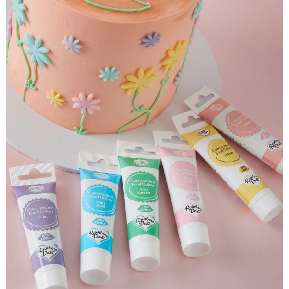 Ein pfirsichfarbener Kuchen mit Blumen und sechs Tuben Lebensmittelfarbe.