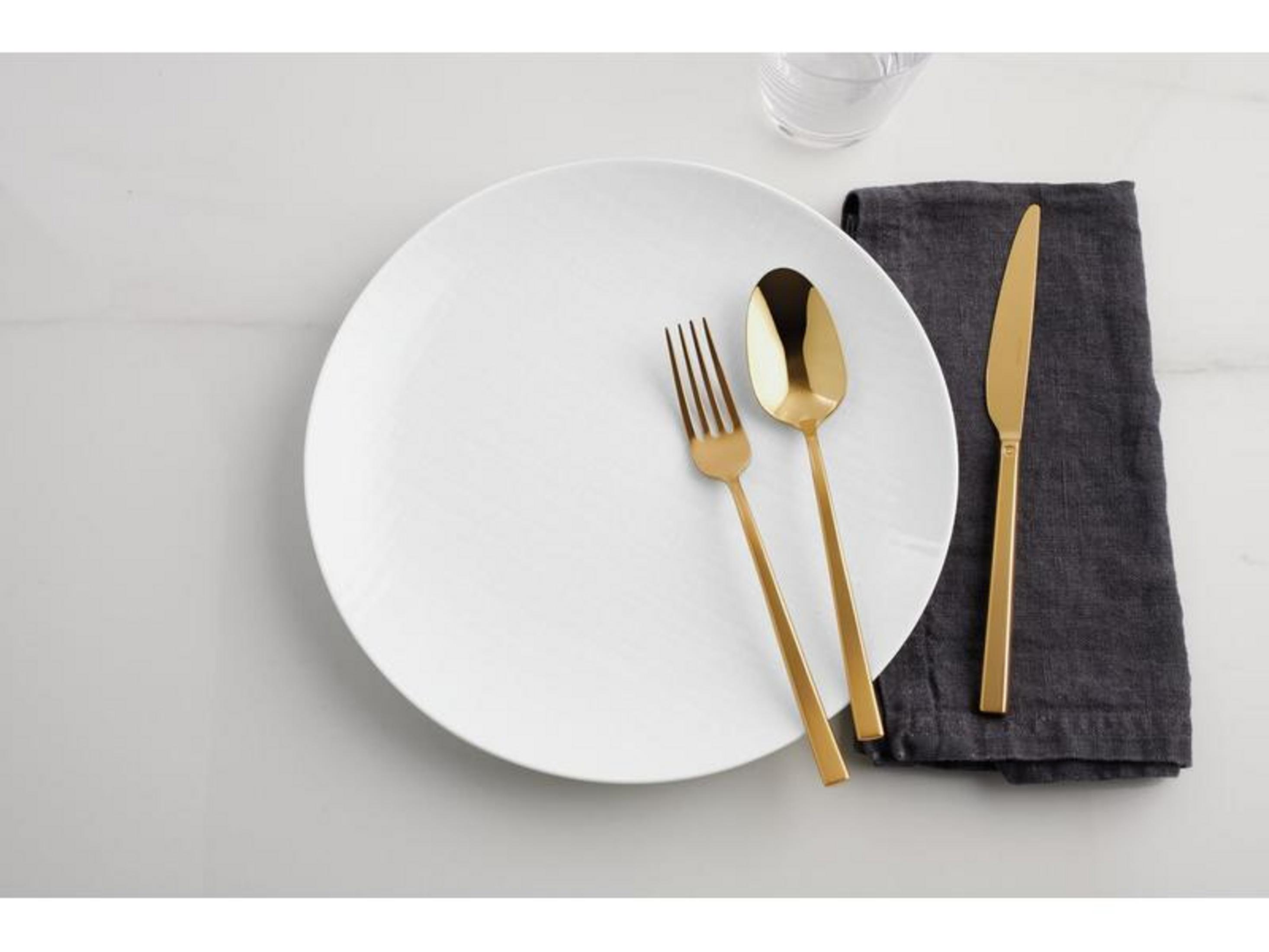 Une assiette blanche avec des couverts dorés et une serviette en tissu sombre.