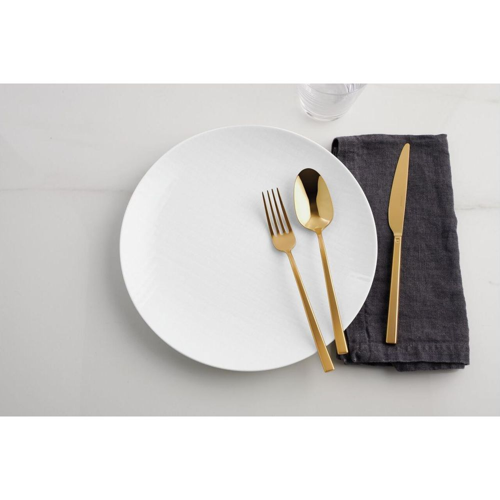 Couverts dorés, fourchette, cuillère et couteau, sur une assiette blanche avec une serviette grise.