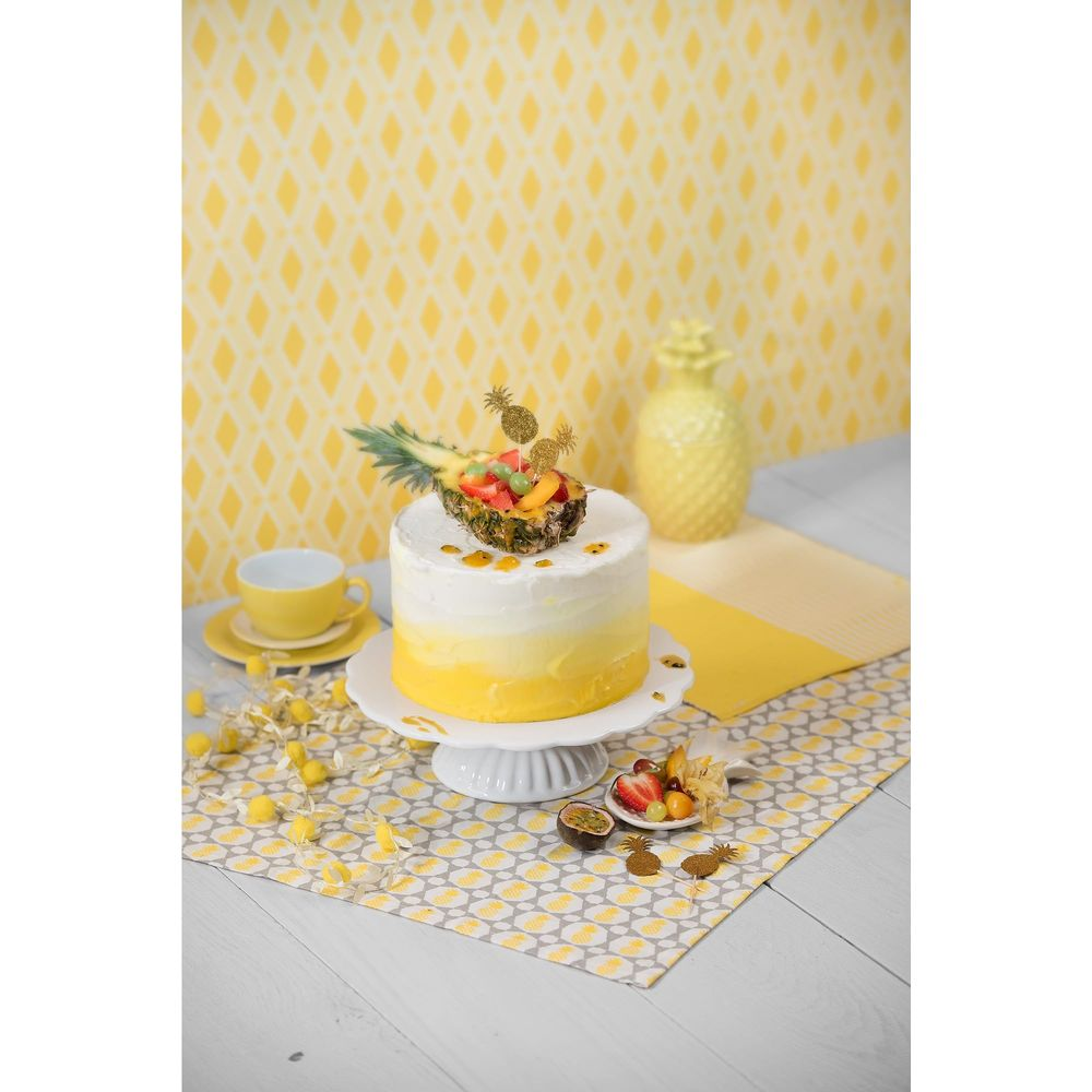 Eine runde Torte mit gelb-weißer Farbverlaufglasur, bekrönt mit einer Ananas-Fruchtschale.