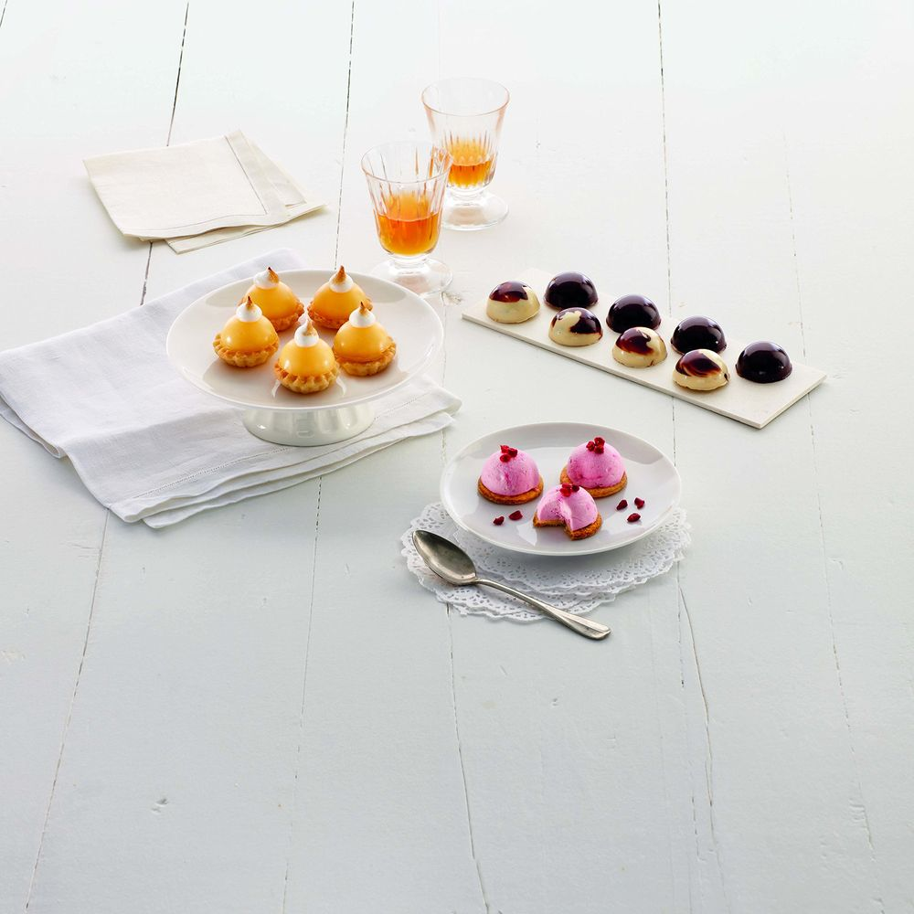 Auswahl an bunten Mini-Desserts und Getränken auf einem weißen Holztisch.