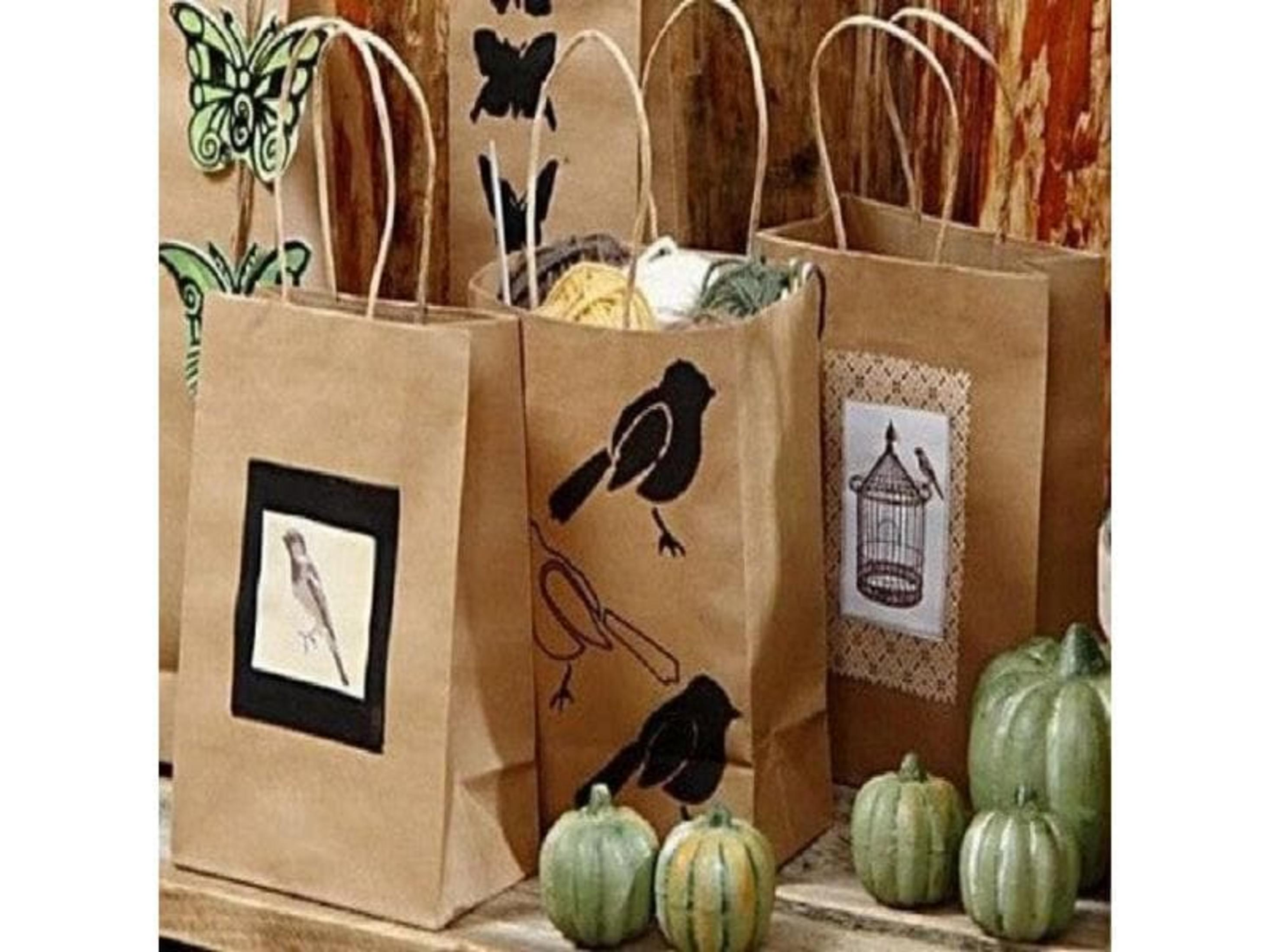 Sacs en papier marron décorés d'oiseaux et de papillons, avec des citrouilles à proximité.