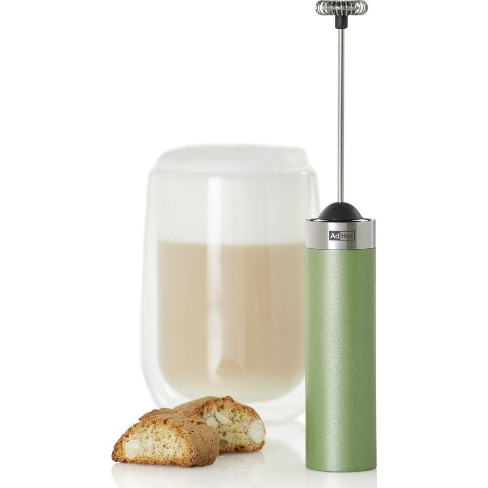 Mousseur à lait vert à côté d'un verre de café et de biscuits.