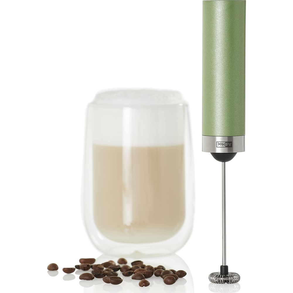 Un verre de café au lait avec mousse et un mousseur à lait vert avec des grains de café.