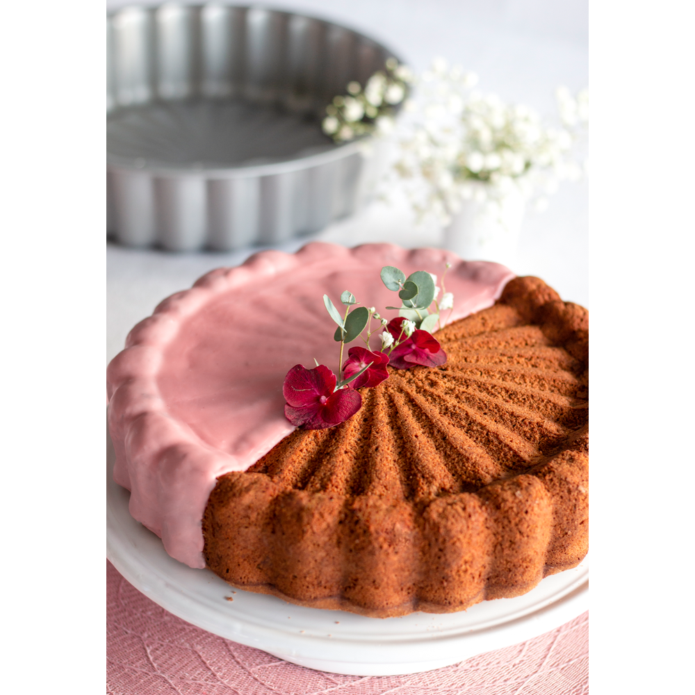 Ein Kuchen mit rosa Glasur und Beeren, dekoriert mit grünen Blättern.