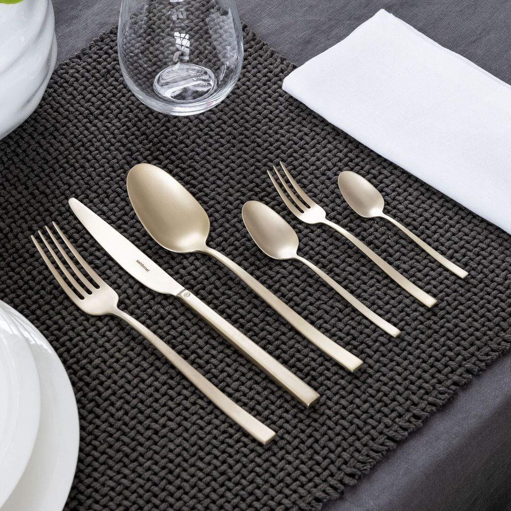 Ein Set aus gebürstetem Goldbesteck ist auf einer dunkelgrauen Tischset mit weißer Serviette arrangiert.