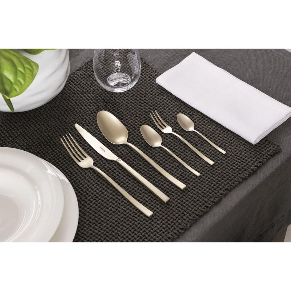 Ein goldfarbenes Besteckset mit Tellern, Glas und Serviette auf dunkler Matte.