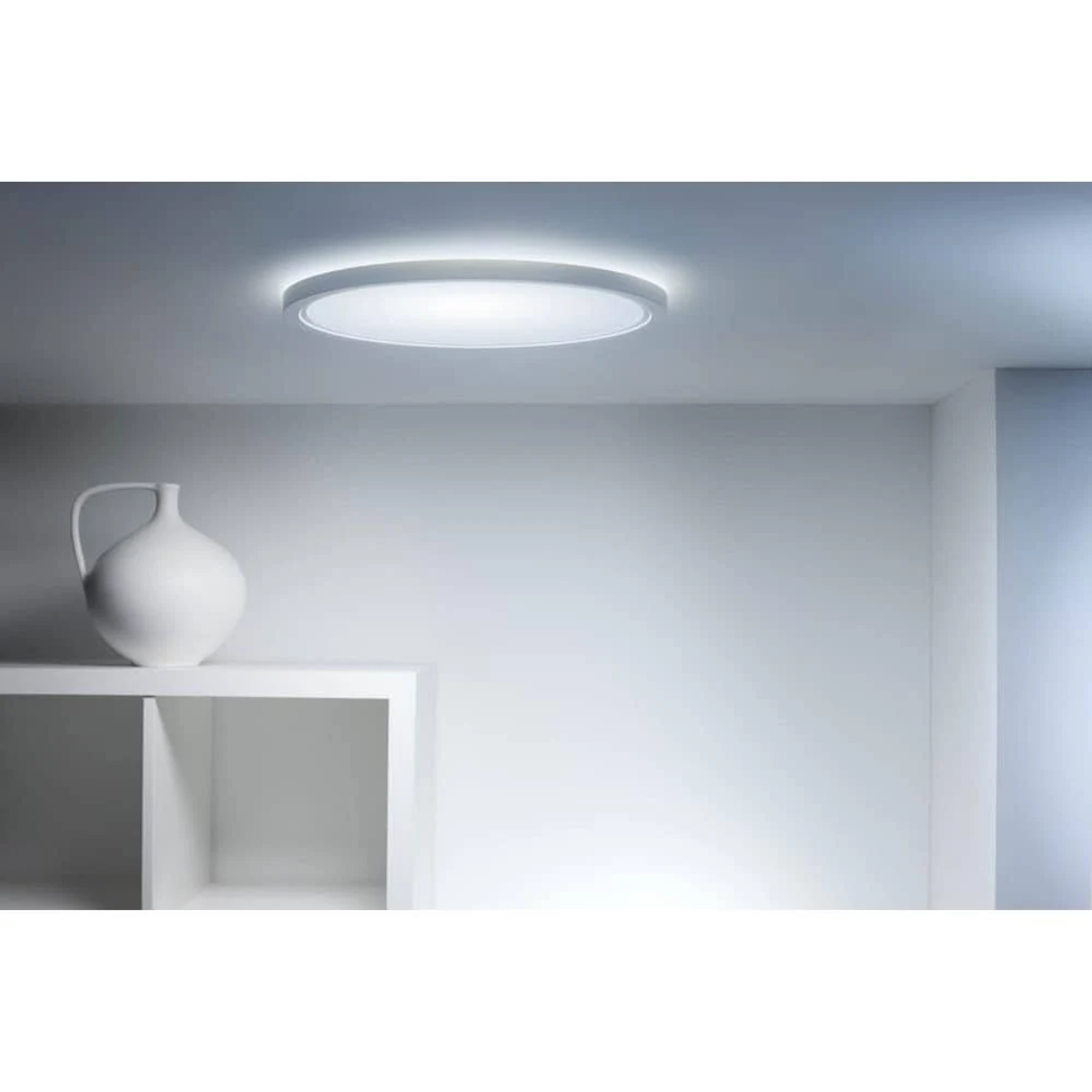 Un vase blanc sur une étagère sous un plafonnier circulaire.