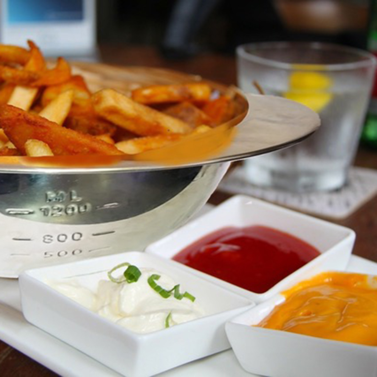 Patatas fritas con tres salsas: kétchup, mayonesa y salsa de queso. Un vaso de agua.