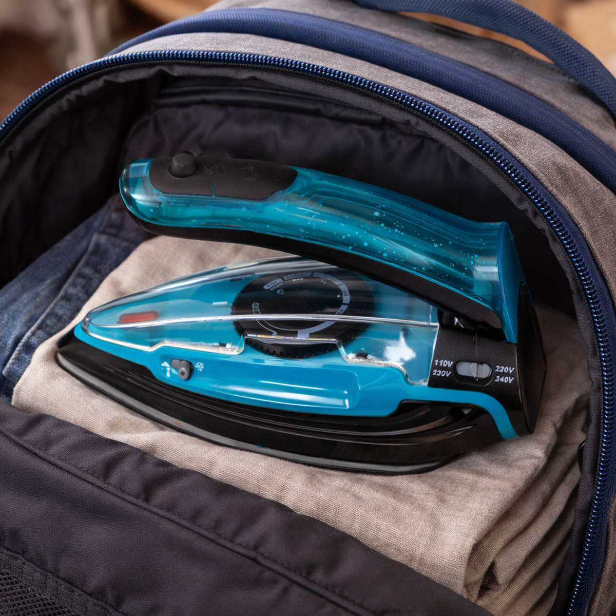 Una plancha de viaje azul descansa sobre ropa doblada dentro de una mochila.