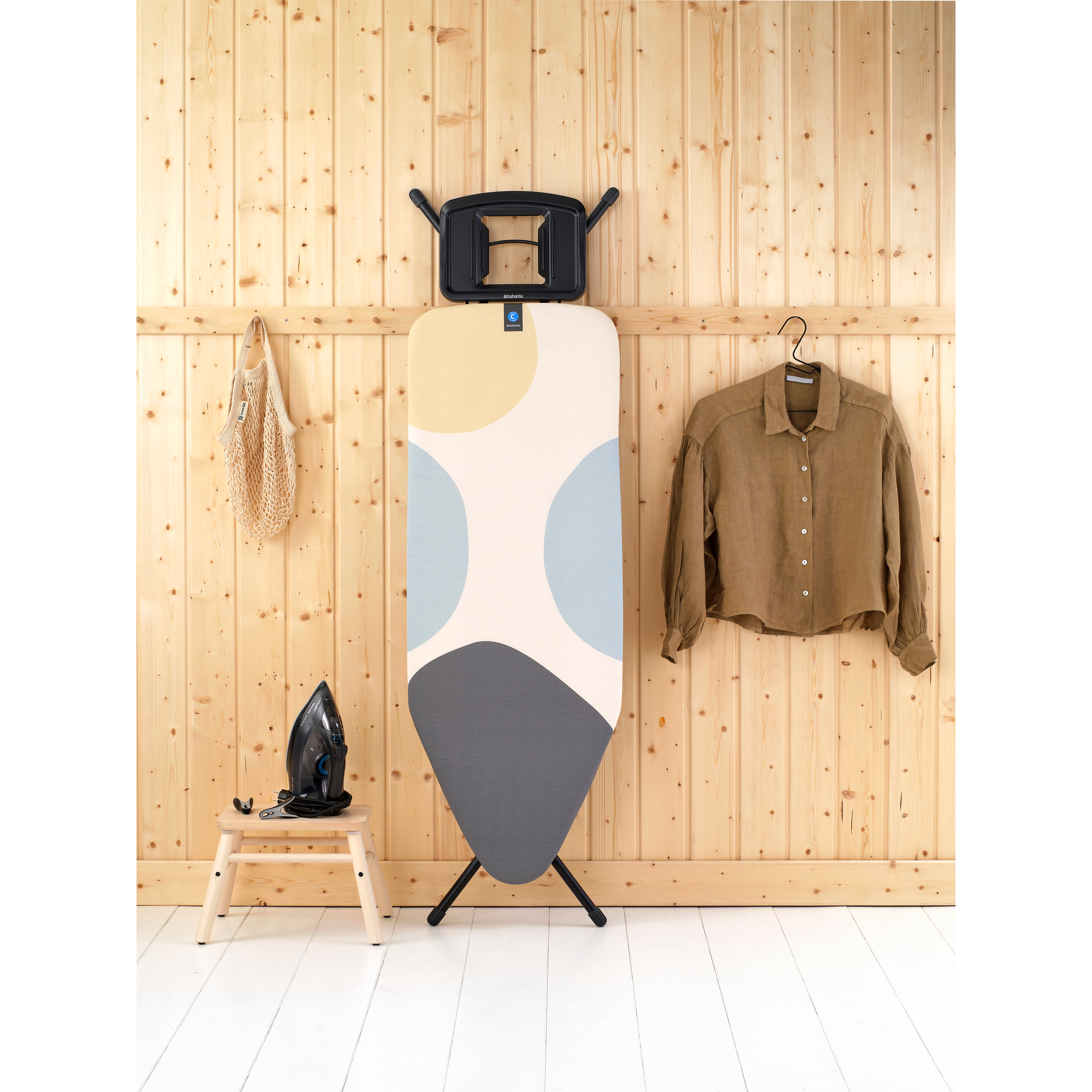 Bügeleisen auf einem Hocker, Bügelbrett und Hemd an Holzwand.