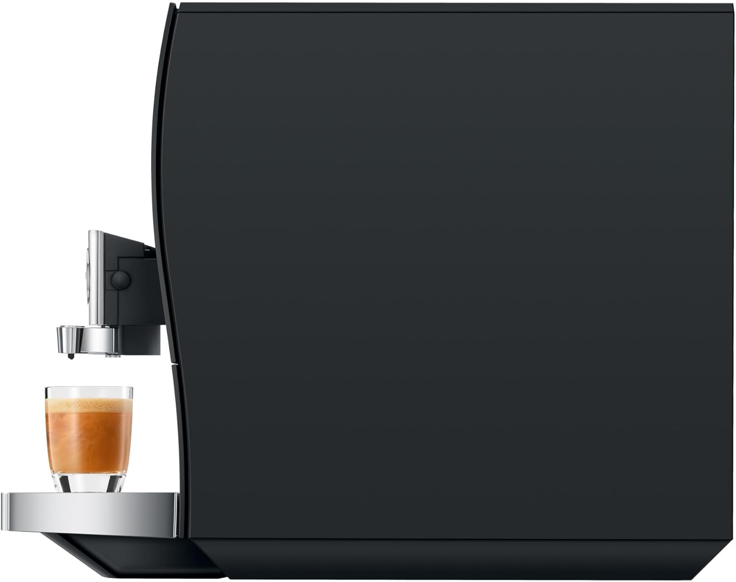 Un bicchiere di espresso con schiuma cremosa si trova su una vaschetta raccogligocce davanti a una macchina da caffè nera.