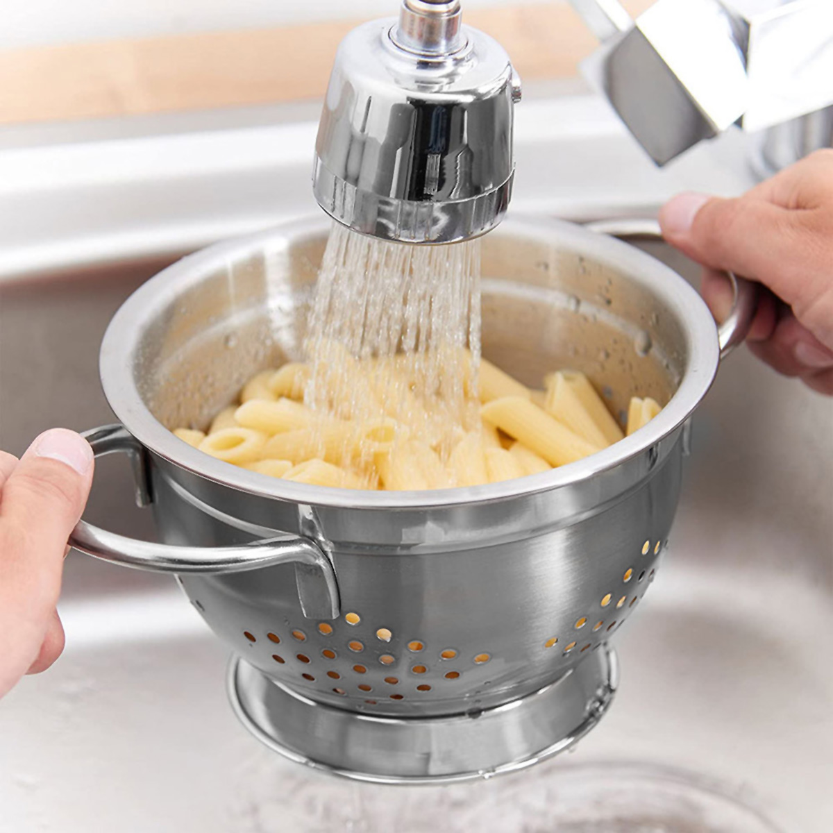La pasta penne se enjuaga en un colador bajo agua corriente.