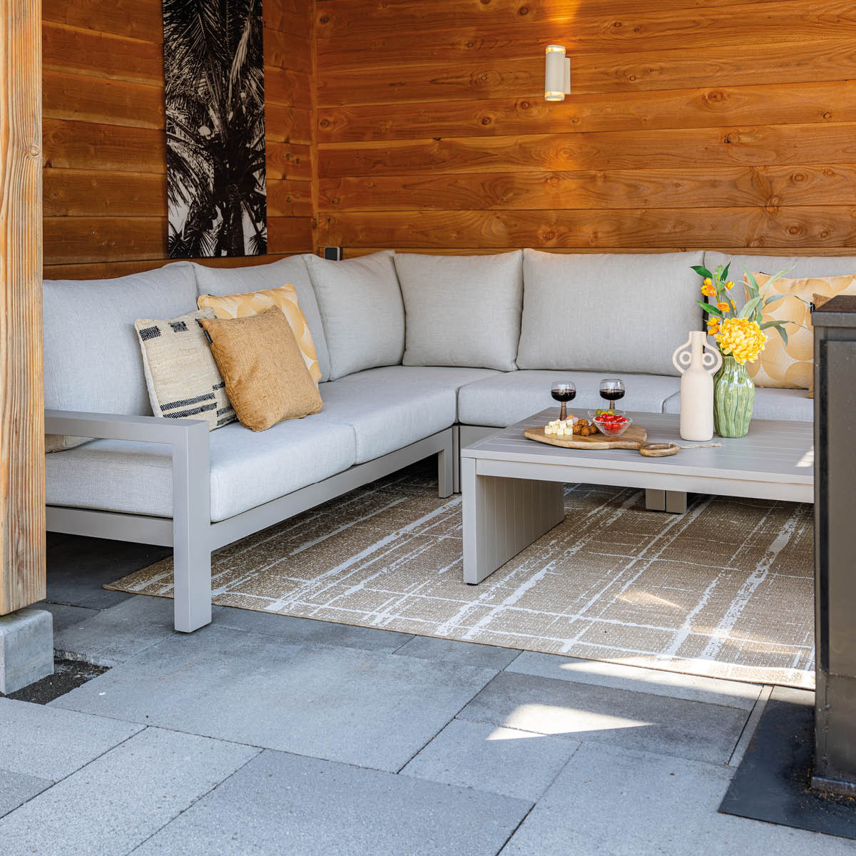 Gray sectional sofa with cushions and coffee table with snacks and wine. Wooden wall.