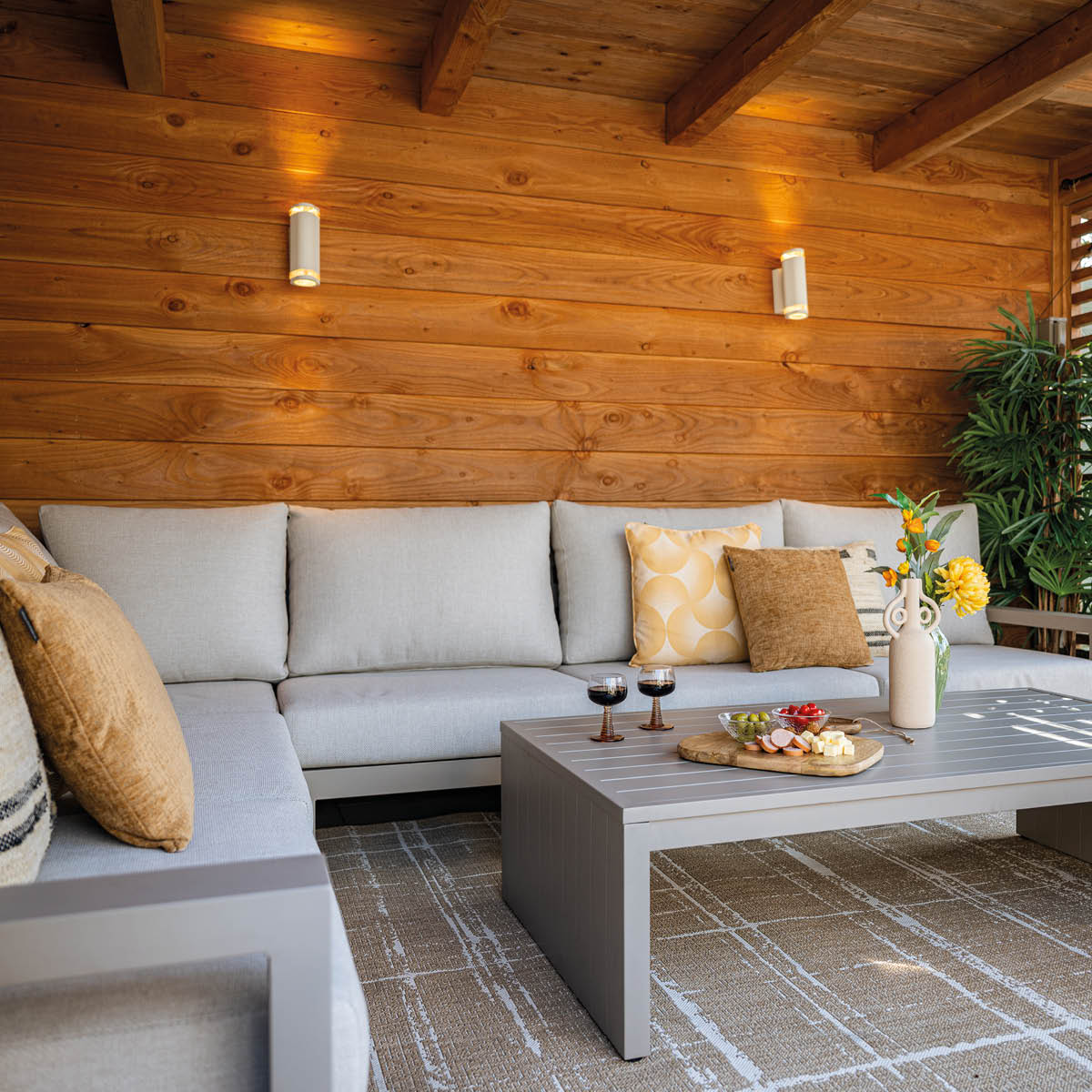 A modern sectional sofa with pillows, coffee table with snacks, and a vase of flowers.