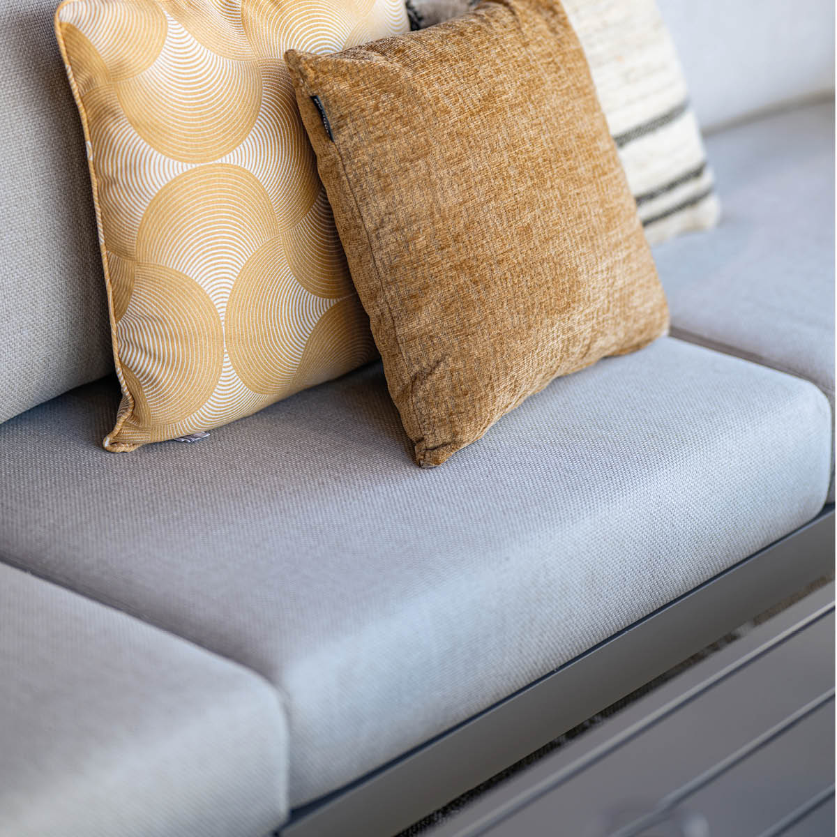 Three pillows on a light grey sofa. One with a geometric pattern, two solid colored.