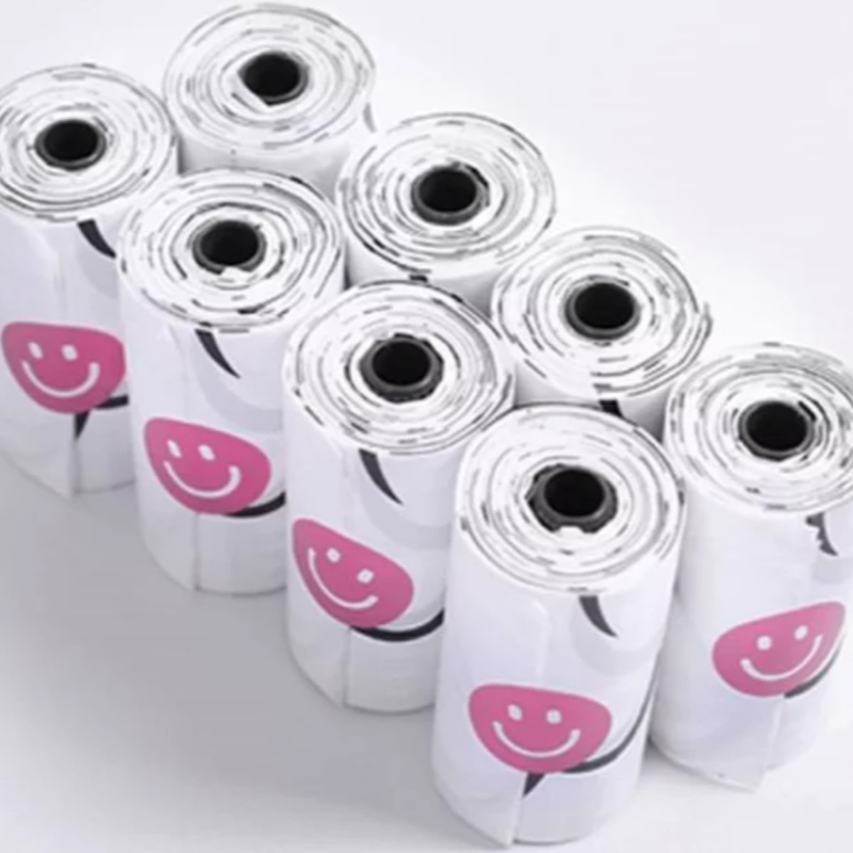 Diversi rotoli di sacchi della spazzatura con facce sorridenti rosa su sfondo bianco.