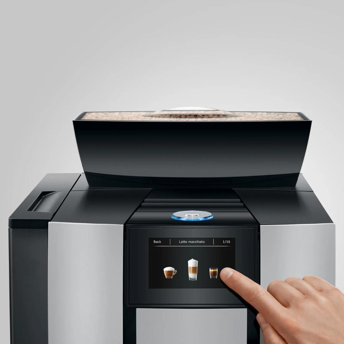 Una mano seleziona Latte Macchiato sul touchscreen di una macchina da caffè.