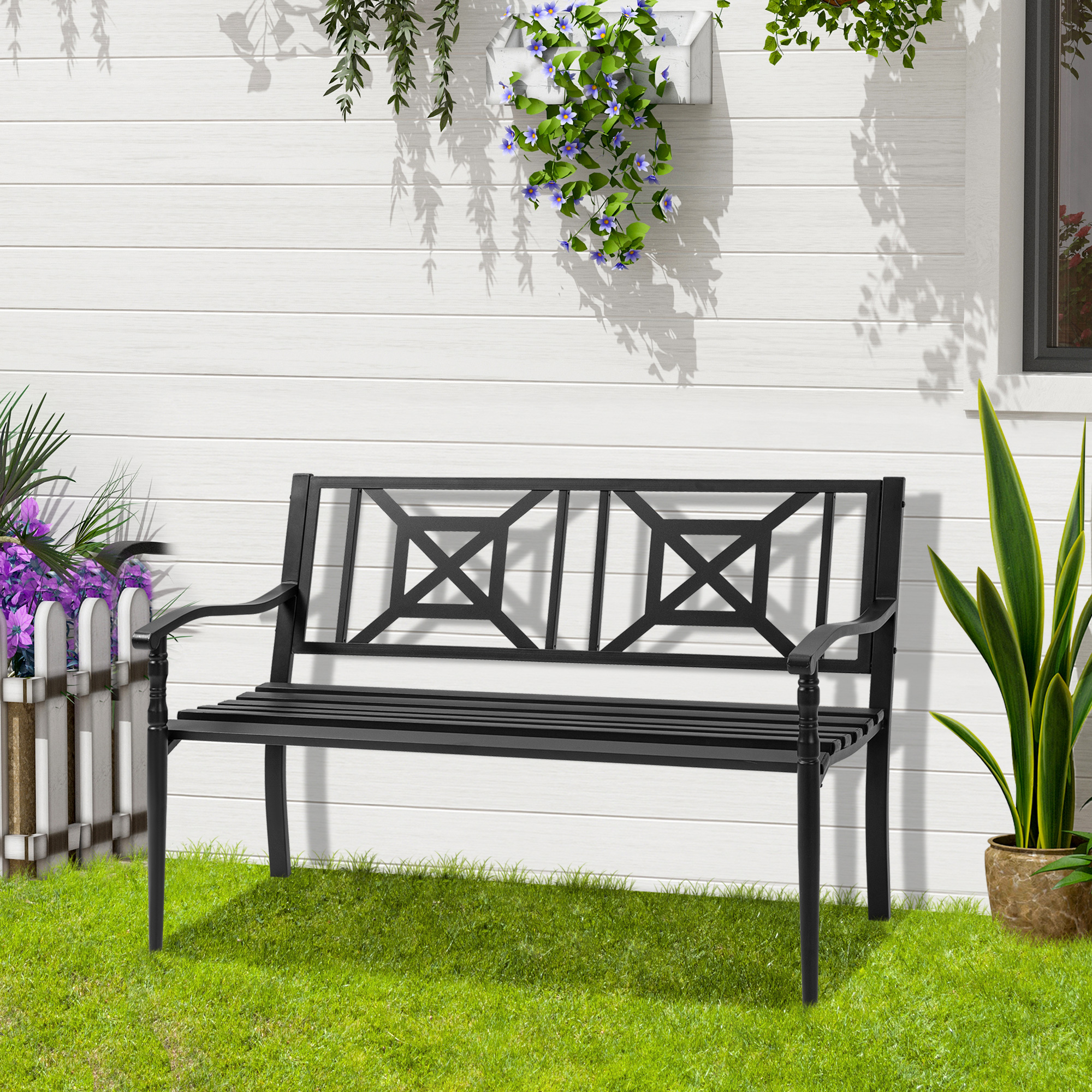 Una panchina da giardino nera davanti a un muro di legno bianco con piante e erba.