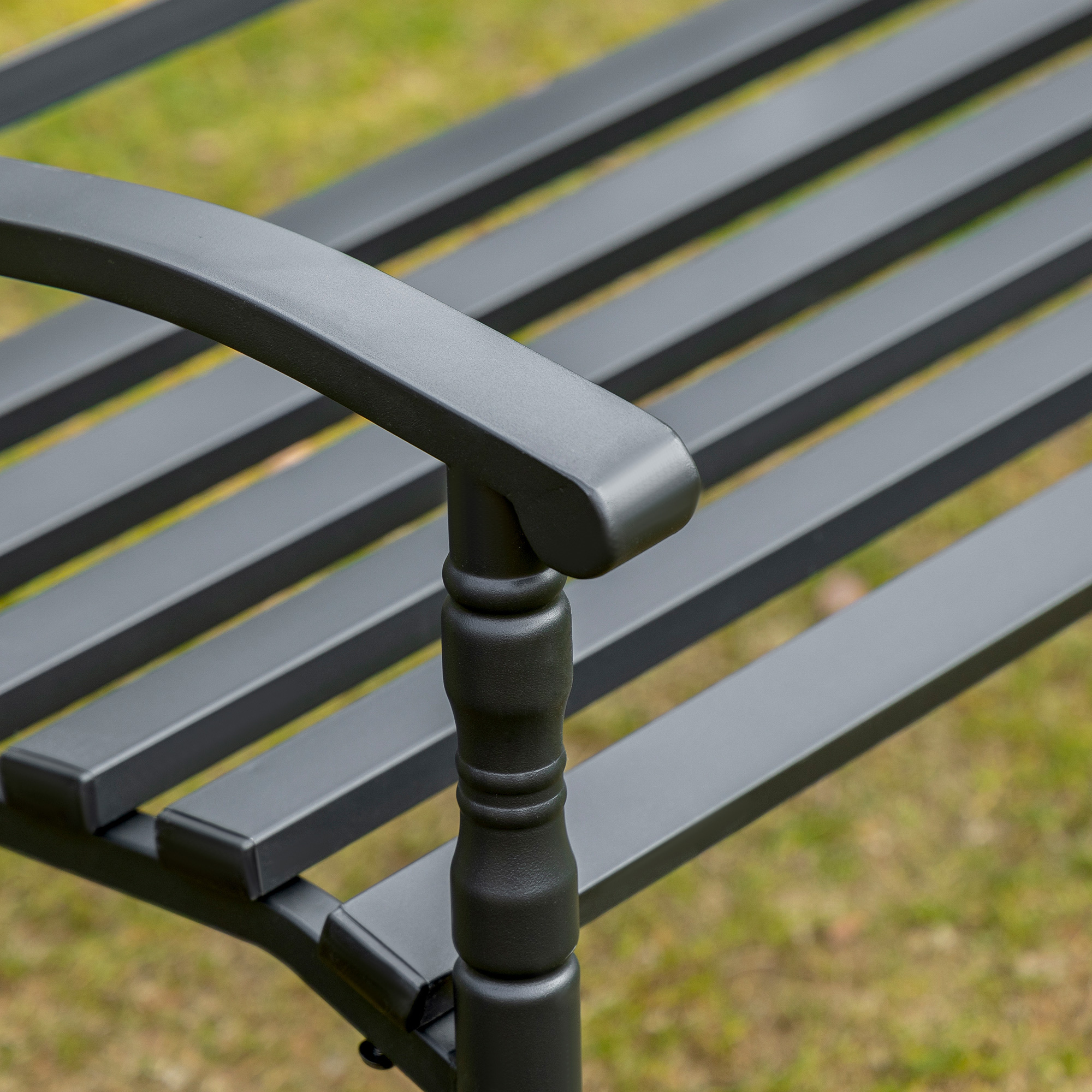 Banco de metal negro con reposabrazos y listones, al aire libre sobre césped.