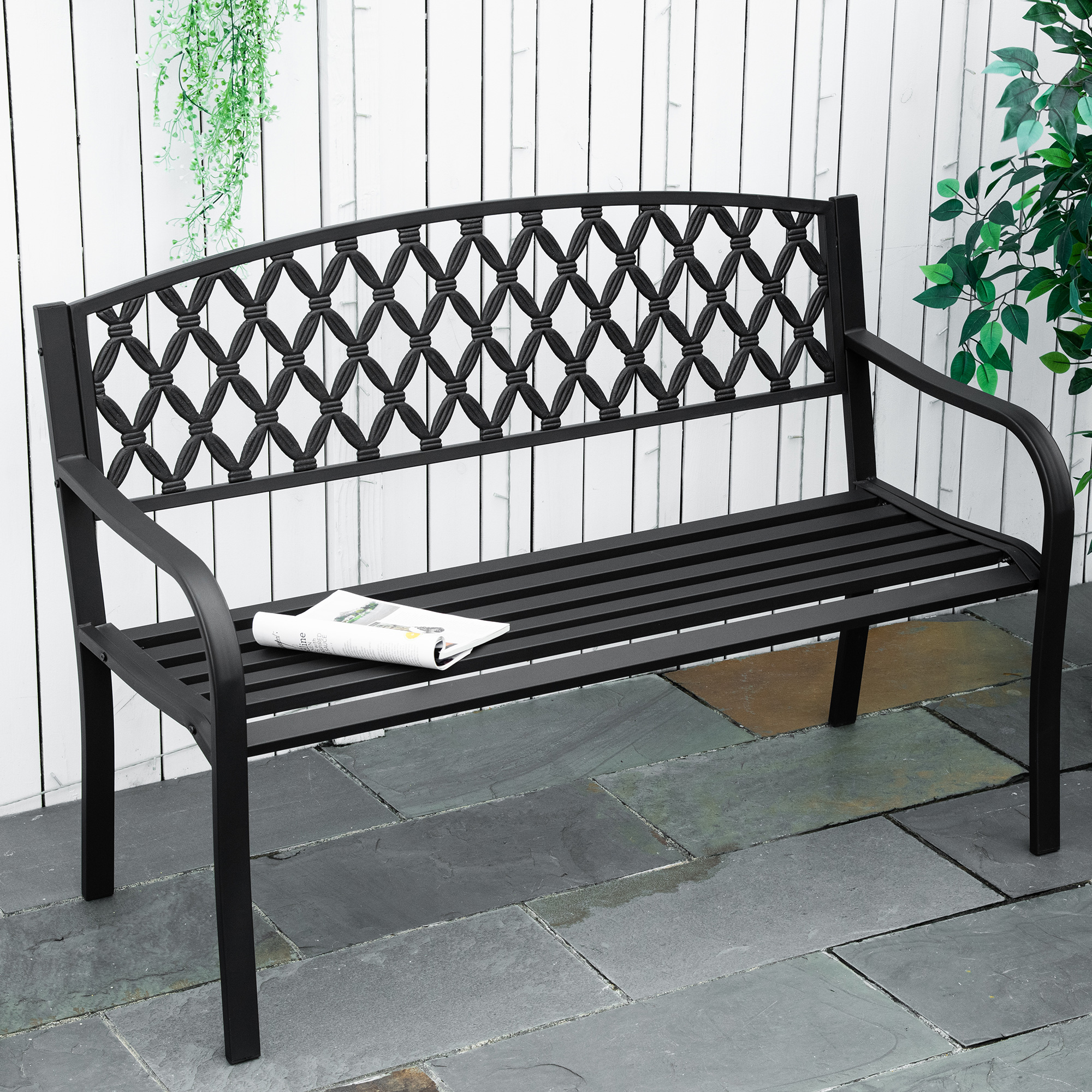 Panchina in metallo nero con schienale decorato e giornale su patio in pietra.