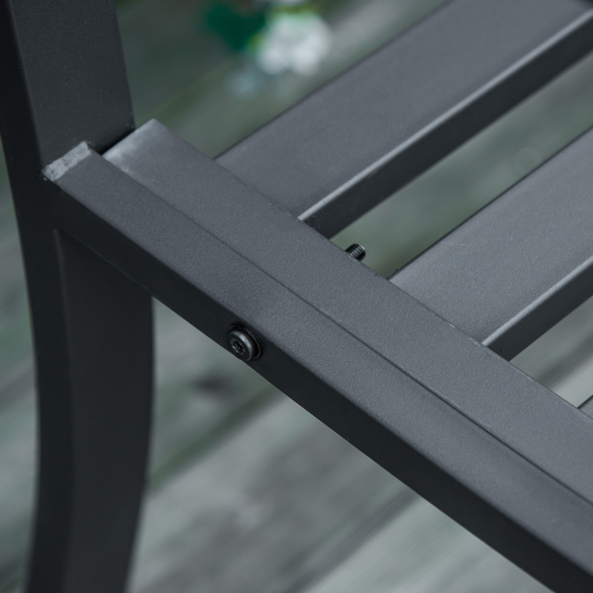 Silla de metal gris con tornillos sobre suelo de madera, fondo borroso.