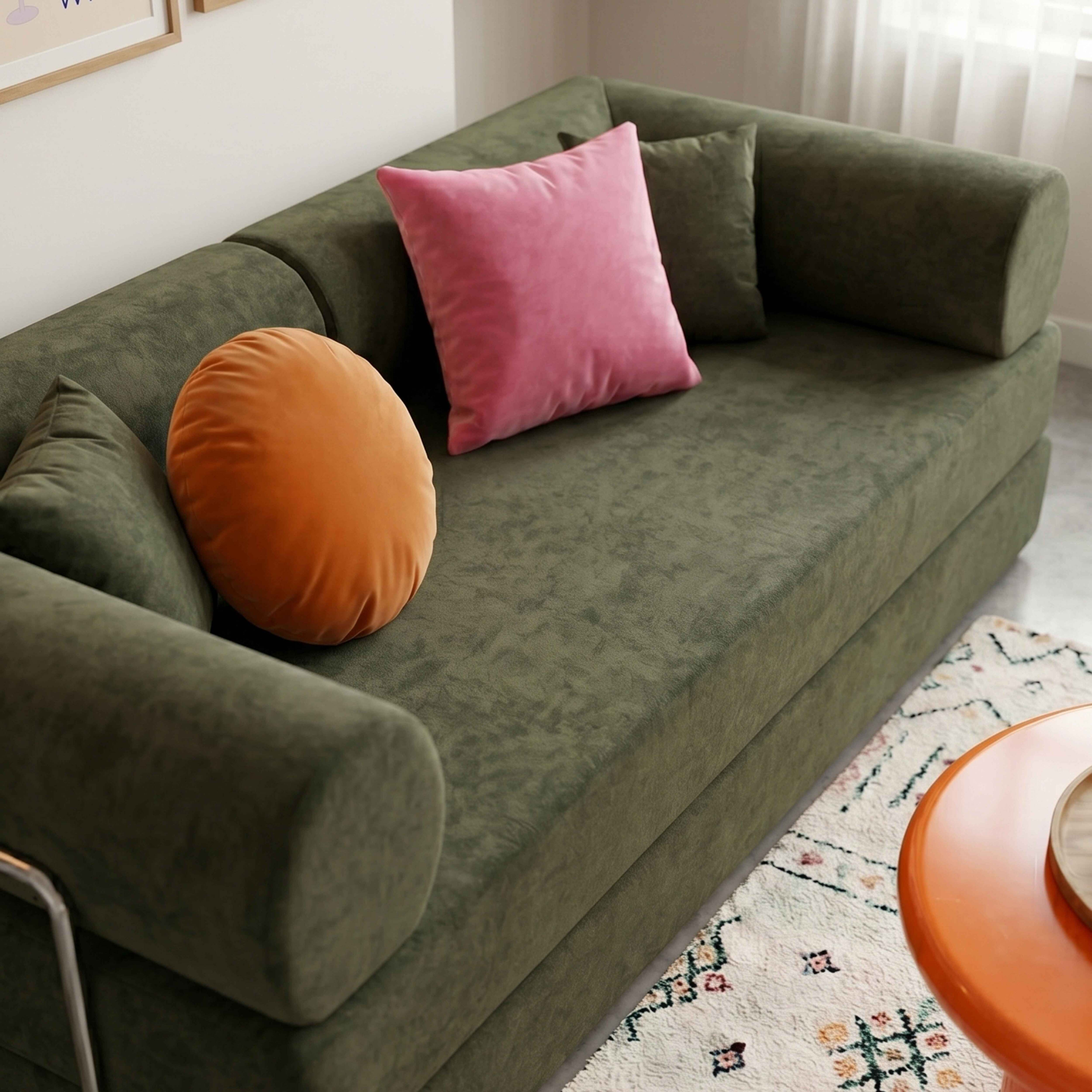 Ein grünes Sofa mit Kissen in Pink und Orange, daneben ein Teppich und ein Tisch.