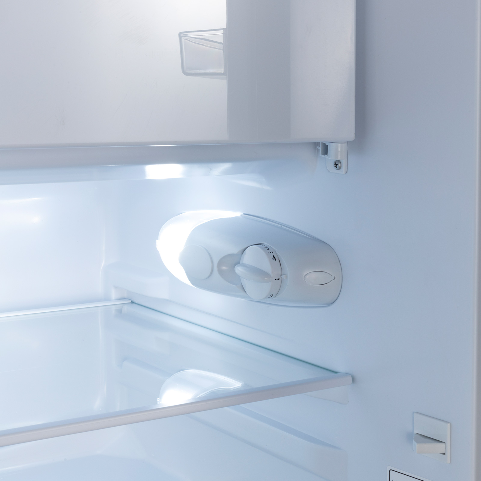 Innenraum eines Kühlschranks mit einem weißen Thermostatregler und Glasböden.