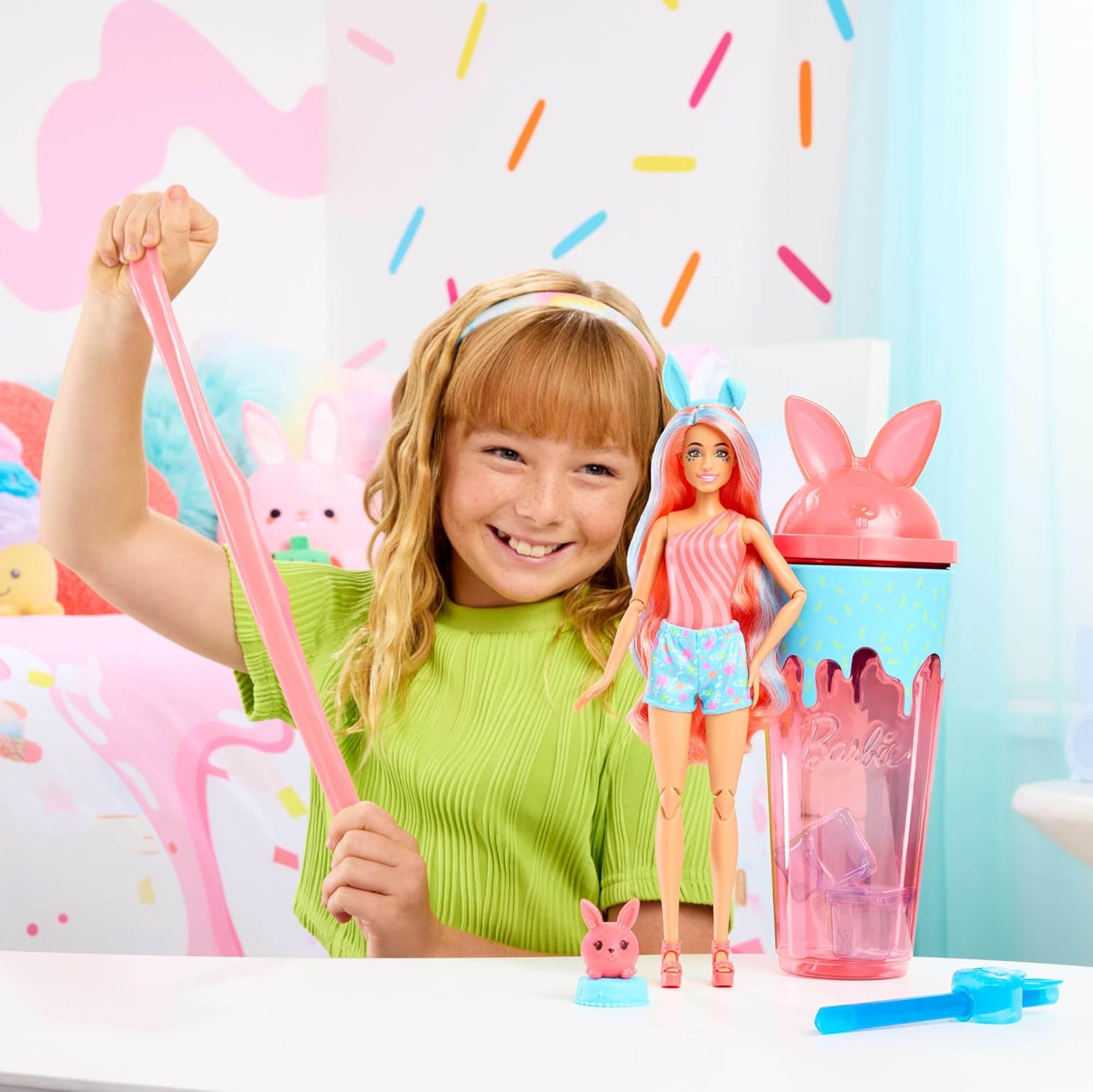 Mädchen spielt mit pinkem Schleim neben Barbie-Puppe und Hasenbecher.