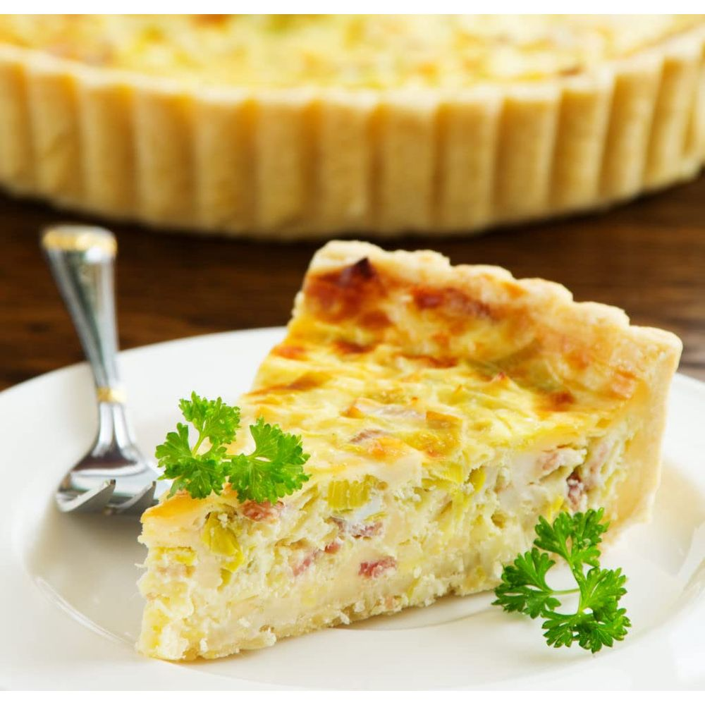 Kawałek quiche z porem i boczkiem na talerzu, udekorowany natką pietruszki.