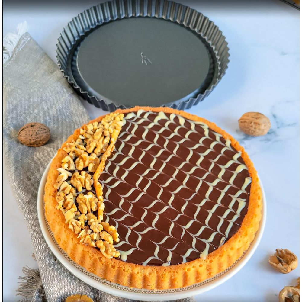 Tarta czekoladowa z orzechami i lukrem, obok formy do tarty.