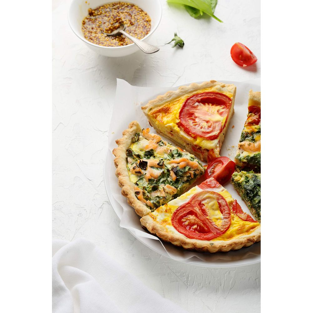 Plastry quiche z łososiem, szpinakiem i pomidorem na białym talerzu.