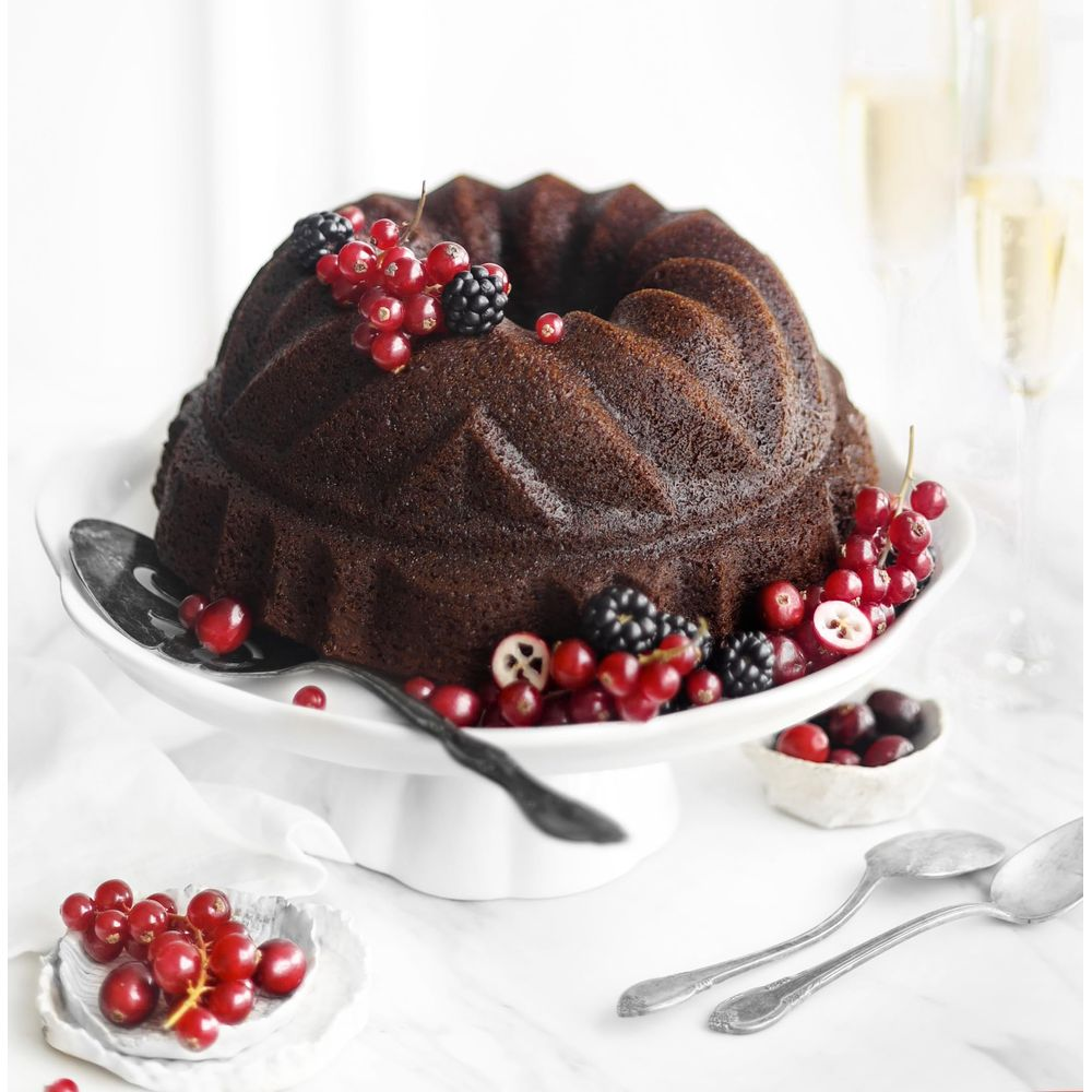 Ciemne ciasto bundt z jagodami i łyżkami do serwowania na stojaku.