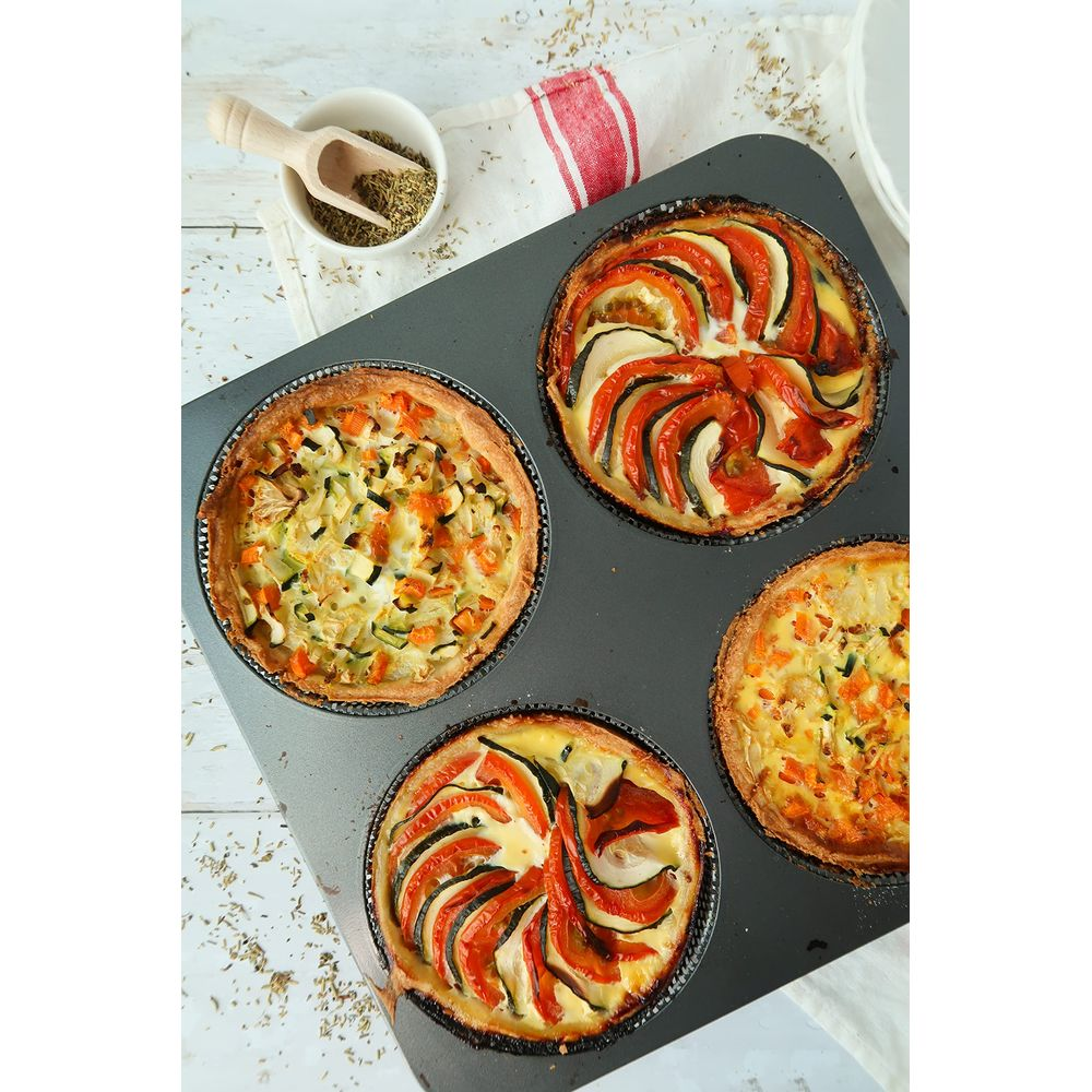 Cztery mini quiche w formie do muffinek, ozdobione warzywami i ziołami.