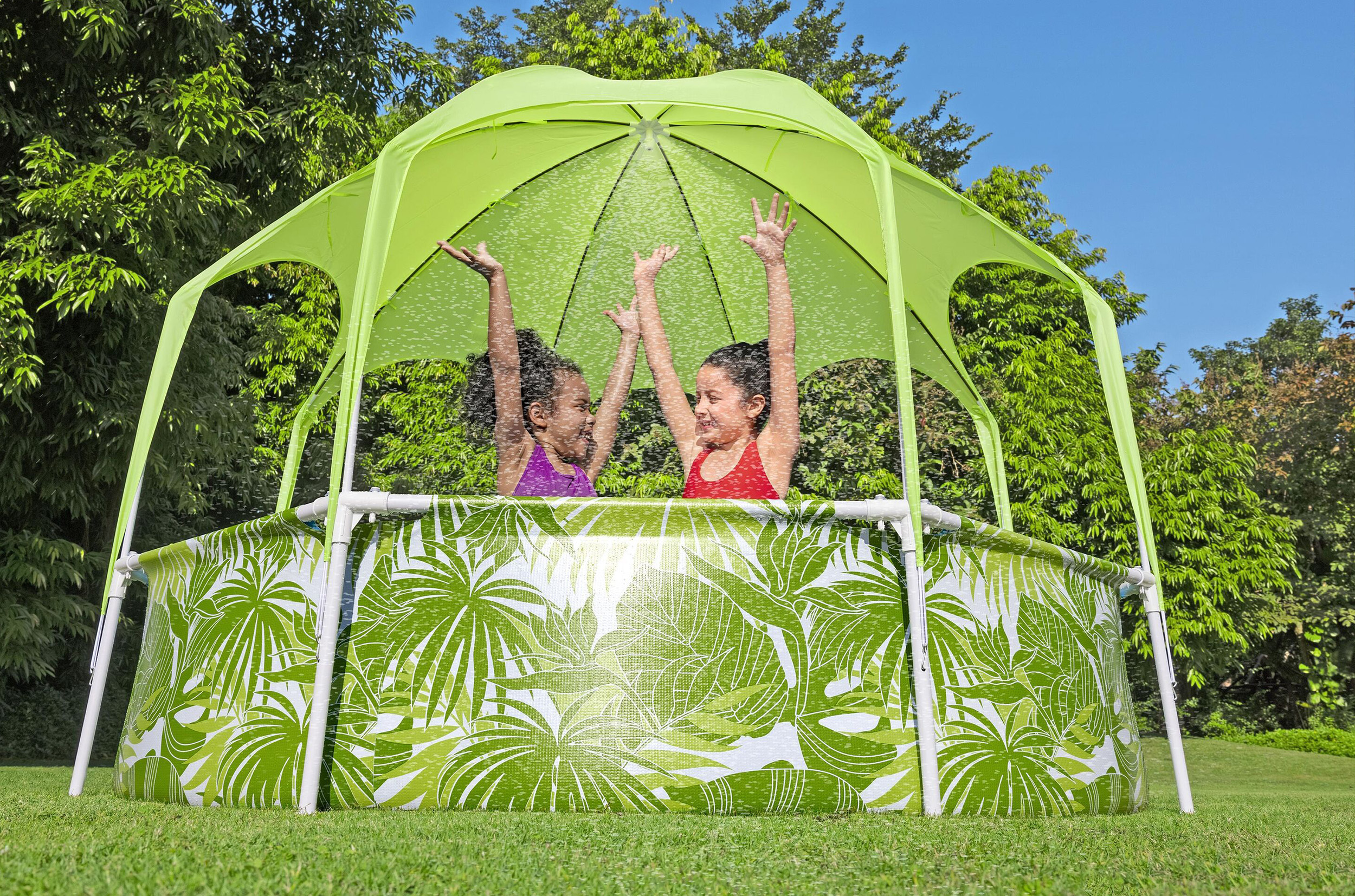 Due bambine in una piscina con parasole verde e nebbiolina d'acqua.