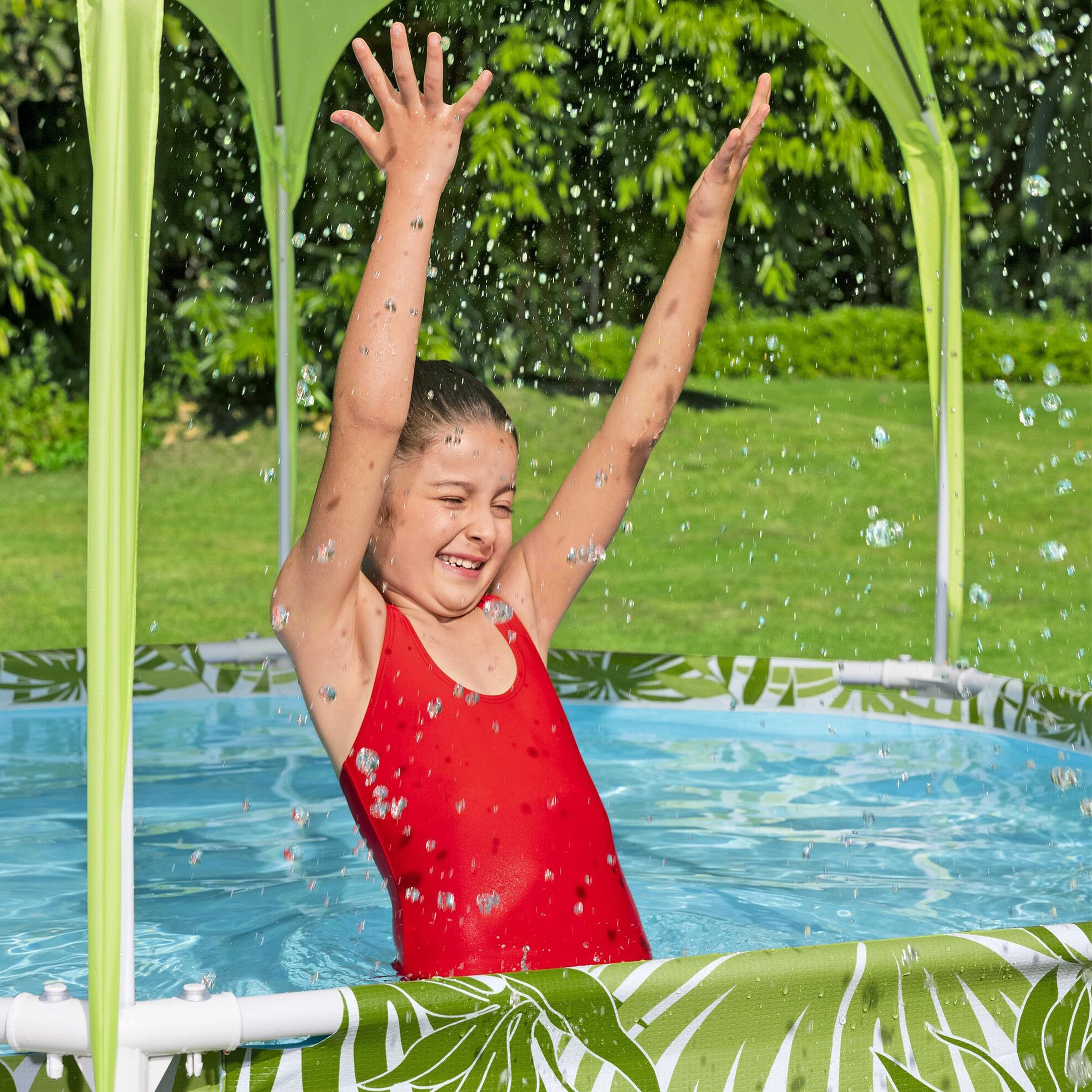 Una ragazza in costume da bagno rosso ride con le braccia alzate in una piscina con tettoia verde.